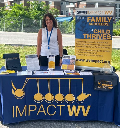 Vicki Johnson standing behind a table decorated with Impact WV literature and informational presentation board